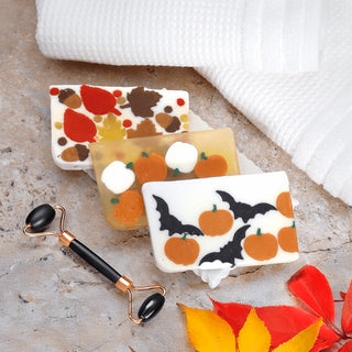Three soap bars with autumn-themed designs and a black and gold roller on a light surface.