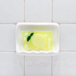 California Lemon Vegetable Glycerin Bar Soap in a white soap dish on a tiled bathroom wall.