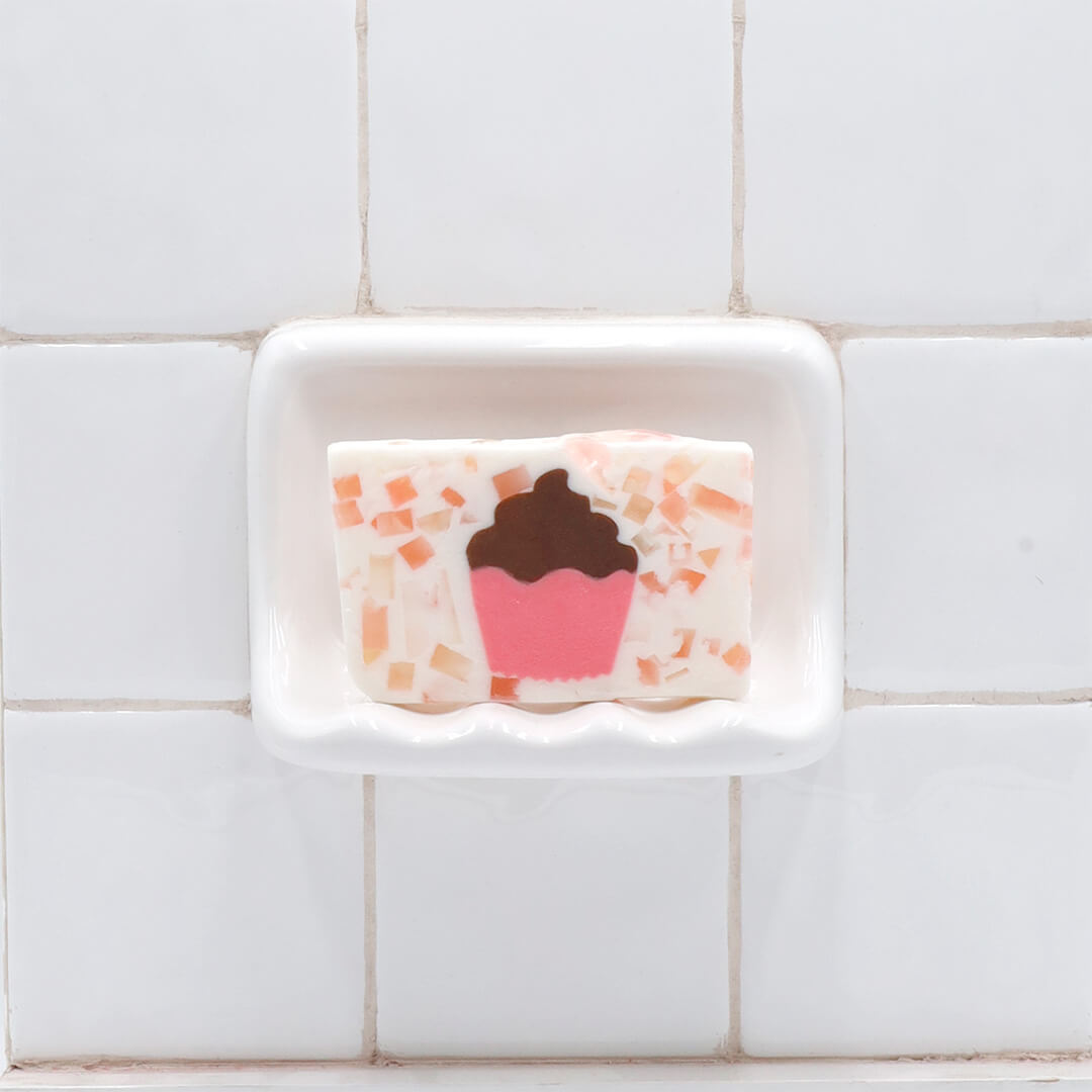 Cupcake Vegetable Glycerin Bar Soap in a white soap dish on a tiled bathroom wall.