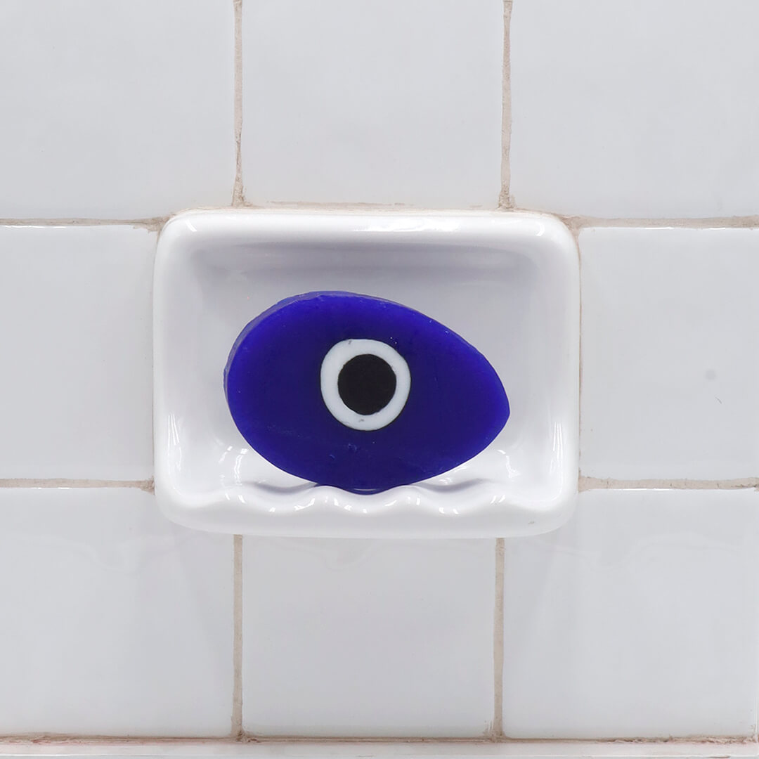 Evil Eye Vegetable Glycerin Bar Soap in a white soap dish on a tiled bathroom wall.