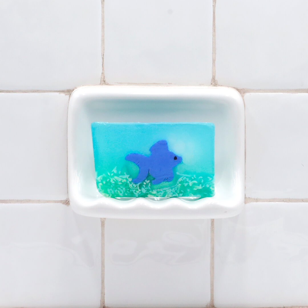 Ginger Fish Vegetable Glycerin Bar Soap in a white soap dish on a tiled bathroom wall.