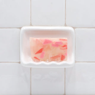 Himalayan Pink Sea Salt Vegetable Glycerin Bar Soap in a white soap dish on a tiled bathroom wall.