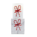 A white glass candle jar with a red and white candy cane bow illustration, displayed on top of its white marble-patterned box, which also features the same design and the brand name 'ICON CANDLE'.
