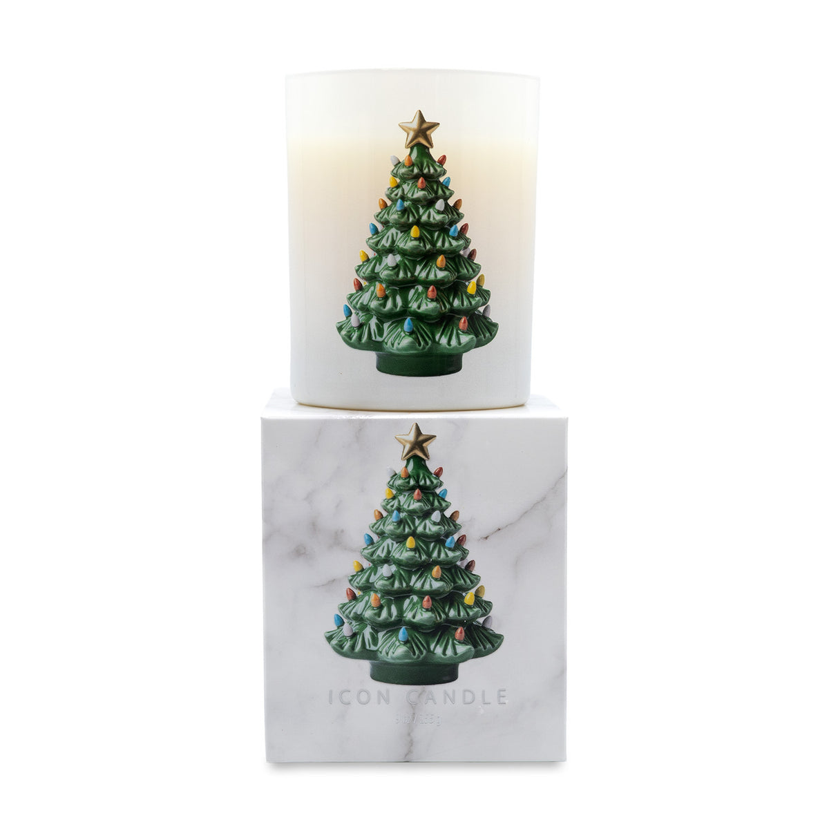 A lit white scented candle in a cylindrical glass holder, stacked above its white marble-patterned box. Both the candle and packaging feature a green Christmas tree ornament with colorful lights and a gold star on the front.