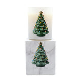 A lit white scented candle in a cylindrical glass holder, stacked above its white marble-patterned box. Both the candle and packaging feature a green Christmas tree ornament with colorful lights and a gold star on the front.