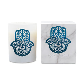 A white glass candle jar with a blue Hamsa hand cutout design, shown next to its white marble-patterned packaging box featuring the same Hamsa design and the text 'ICON CANDLE'.