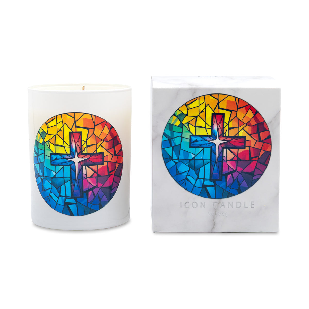 A white wax candle in a cylindrical glass vessel with a colorful stained-glass-style cross design, shown next to its white marble-texture branded box. The design features a vibrant mosaic of red, orange, yellow, green, blue, and purple tones.