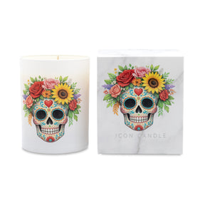 A white candle in a white glass vessel with a colorful sugar skull and floral print, shown next to its white marble-patterned packaging box featuring the same design and the text 'ICON CANDLE'.