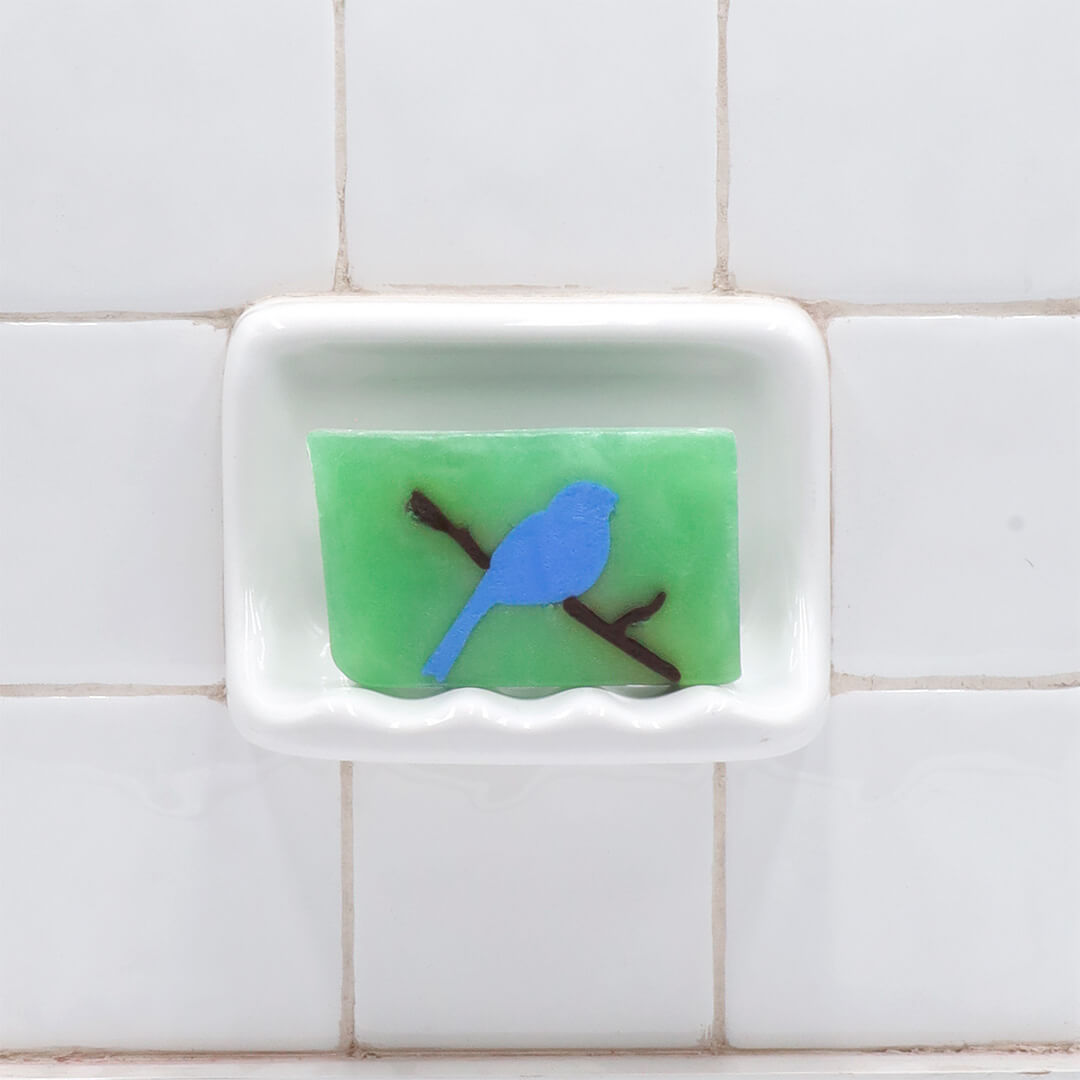 Bluebird glycerin bar soap featuring a soft blue bird perched on a brown branch inside a translucent light green rectangular bar.