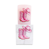 Pink cowboy boots and hat candle on top of a matching white box on a white background.