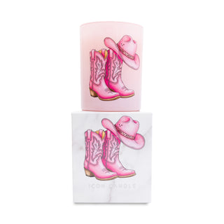 Pink cowboy boots and hat candle on top of a matching white box on a white background.
