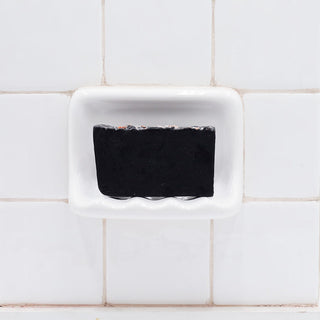 Bamboo Charcoal Vegetable Glycerin Bar Soap in a white soap dish on a tiled bathroom wall.