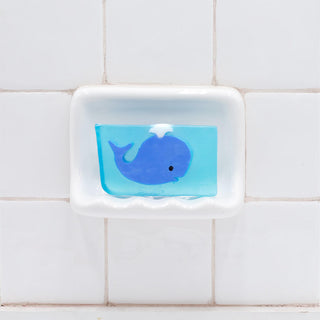 Blue Whale Vegetable Glycerin Bar Soap in a white soap dish on a tiled bathroom wall.