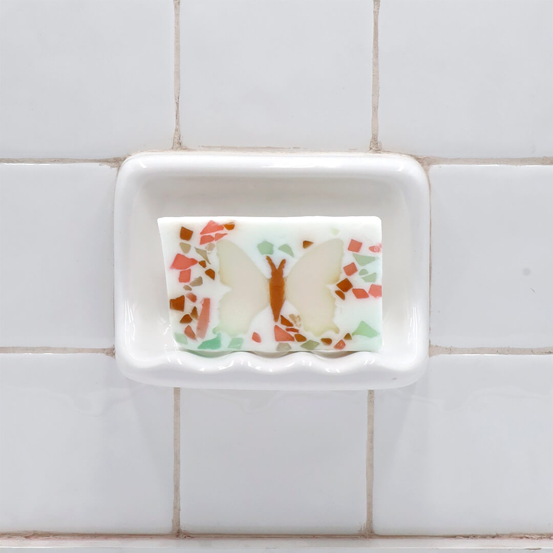 Butterfly glycerin bar soap featuring an ivory butterfly with an orange body surrounded by pink, teal, and pale green soap pieces.