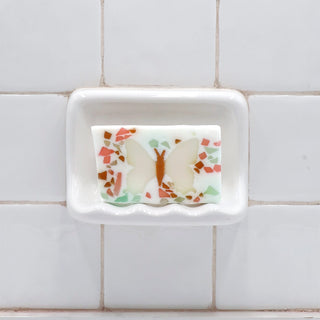Butterfly Vegetable Glycerin Bar Soap in a white soap dish on a tiled bathroom wall.