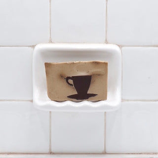 Café Au Lait Vegetable Glycerin Bar Soap in a white soap dish on a tiled bathroom wall.