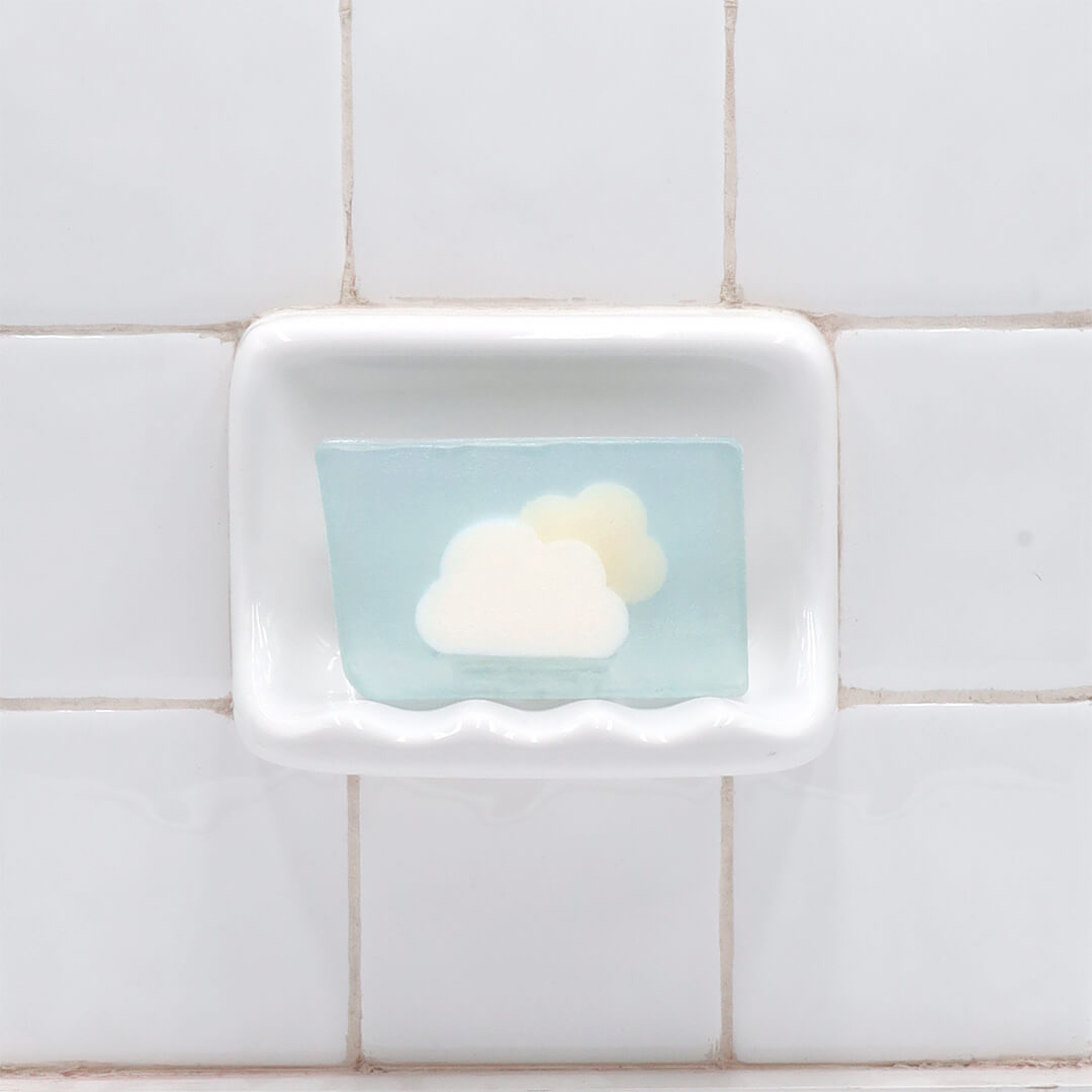 Clouds Vegetable Glycerin Bar Soap in a white soap dish on a tiled bathroom wall.