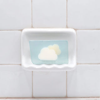 Clouds Vegetable Glycerin Bar Soap in a white soap dish on a tiled bathroom wall.