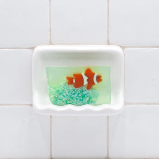 Clownfish Vegetable Glycerin Bar Soap in a white soap dish on a tiled bathroom wall.