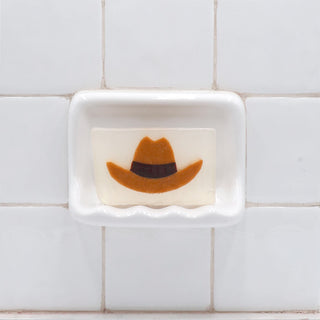 Cowboy Hat Vegetable Glycerin Bar Soap in a white soap dish on a tiled bathroom wall.