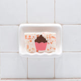 Cupcake Vegetable Glycerin Bar Soap in a white soap dish on a tiled bathroom wall.