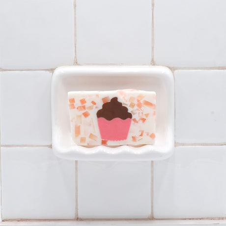 Cupcake Vegetable Glycerin Bar Soap in a white soap dish on a tiled bathroom wall.