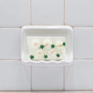 Daisy Vegetable Glycerin Bar Soap in a white soap dish on a tiled bathroom wall.