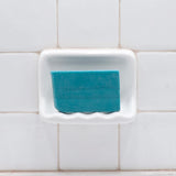 Dead Sea Mud Vegetable Glycerin Bar Soap in a white soap dish on a tiled bathroom wall.