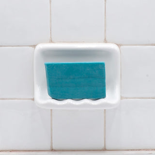Dead Sea Mud Vegetable Glycerin Bar Soap in a white soap dish on a tiled bathroom wall.