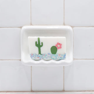 Dos Amigos Vegetable Glycerin Bar Soap in a white soap dish on a tiled bathroom wall.