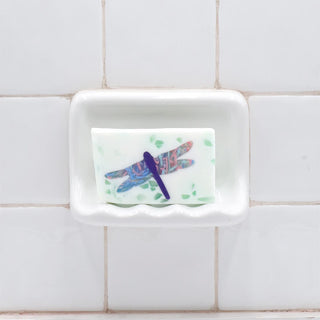 Dragonfly Vegetable Glycerin Bar Soap in a white soap dish on a tiled bathroom wall.