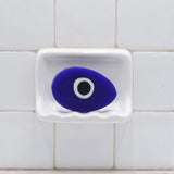 Evil Eye Vegetable Glycerin Bar Soap in a white soap dish on a tiled bathroom wall.