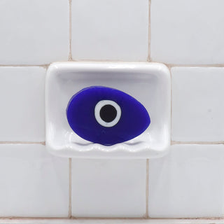 Evil Eye Vegetable Glycerin Bar Soap in a white soap dish on a tiled bathroom wall.