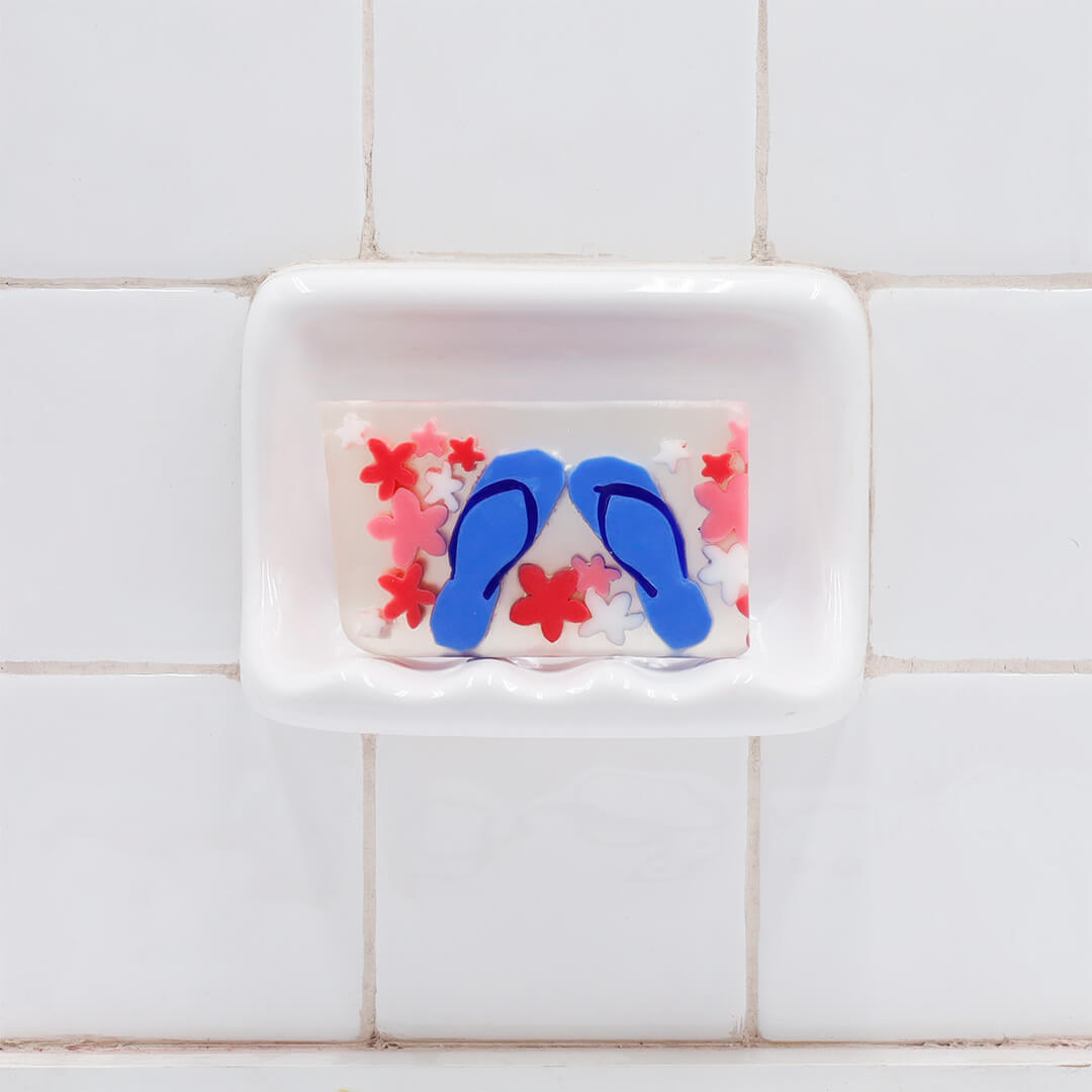 Flip Flops Vegetable Glycerin Bar Soap in a white soap dish on a tiled bathroom wall.