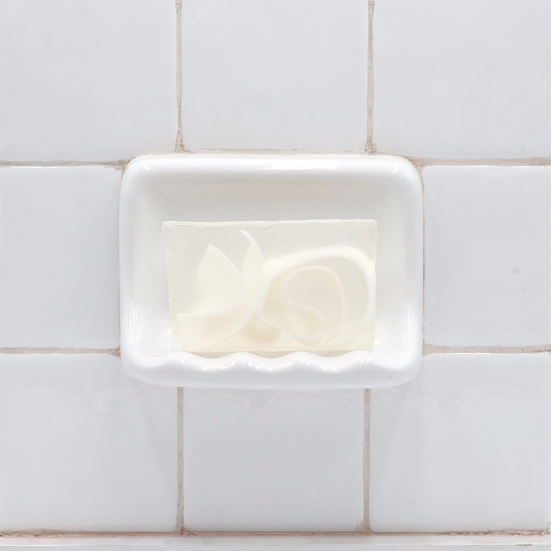 Gardenia Vegetable Glycerin Bar Soap in a white soap dish on a tiled bathroom wall.