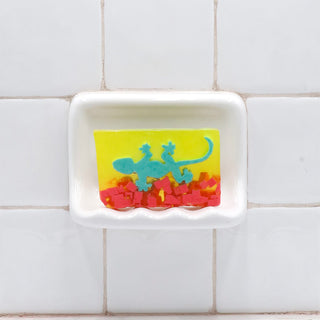 Gecko Vegetable Glycerin Bar Soap in a white soap dish on a tiled bathroom wall.