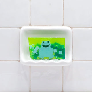 Green Frog Vegetable Glycerin Bar Soap in a white soap dish on a tiled bathroom wall.