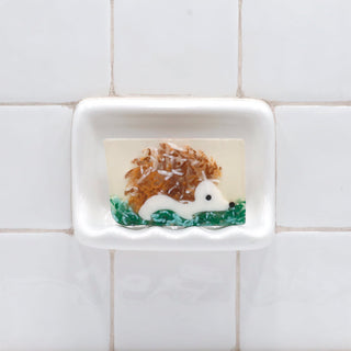 Hedgehog Vegetable Glycerin Bar Soap in a white soap dish on a tiled bathroom wall.