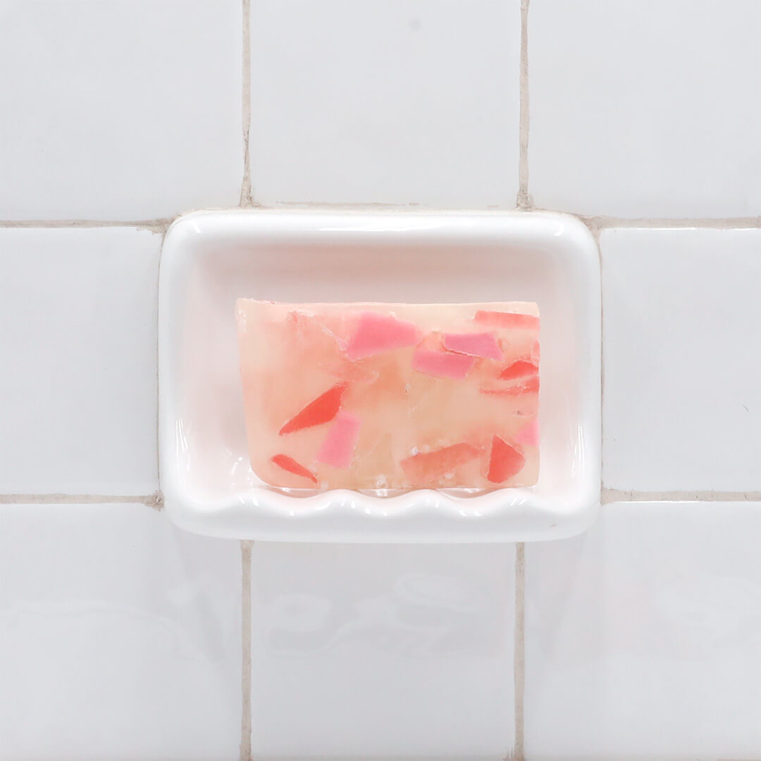 Himalayan Pink Sea Salt Vegetable Glycerin Bar Soap in a white soap dish on a tiled bathroom wall.
