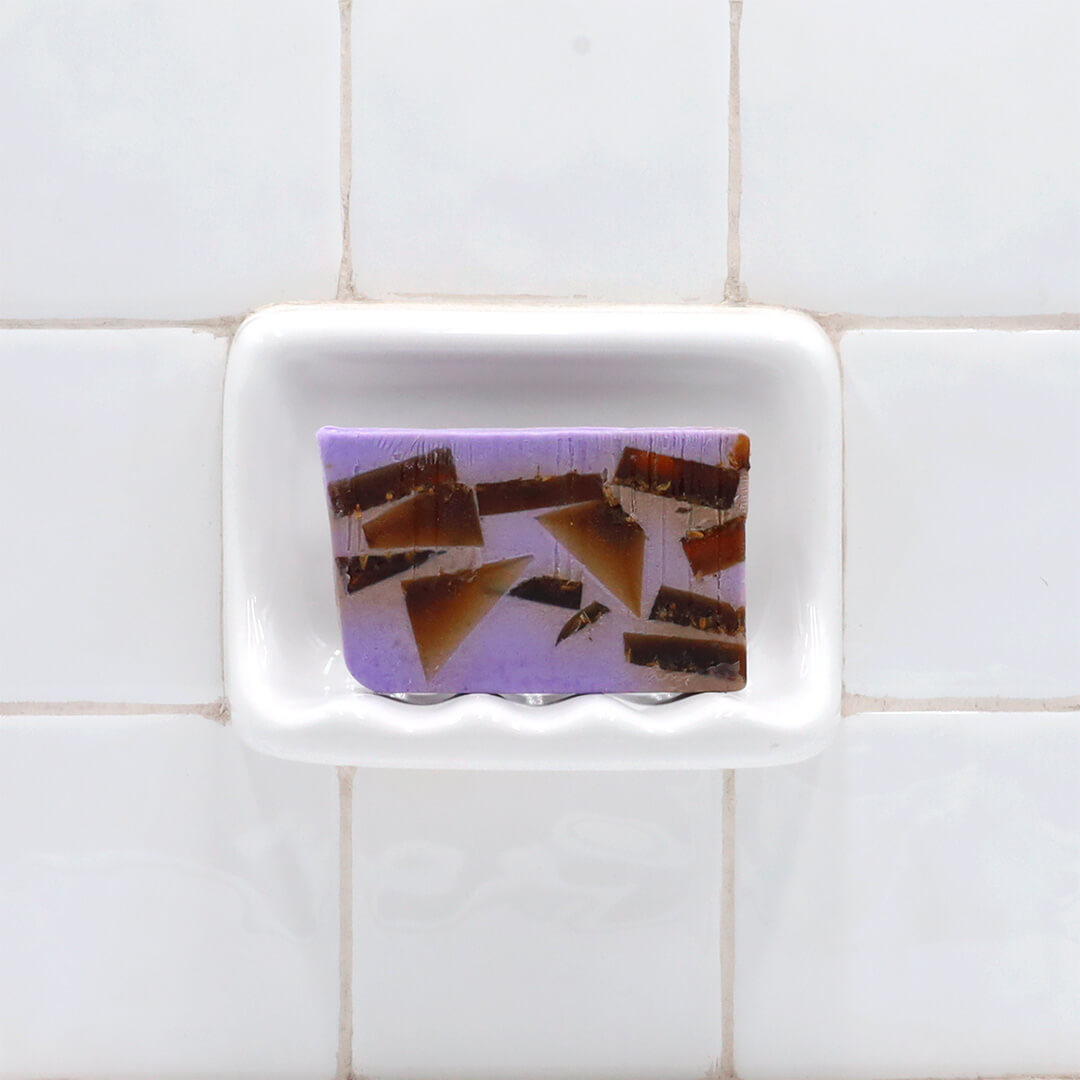 Lavender Essential Oil Vegetable Glycerin Bar Soap in a white soap dish on a tiled bathroom wall.