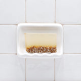 Lavender Oatmeal Vegetable Glycerin Bar Soap in a white soap dish on a tiled bathroom wall.