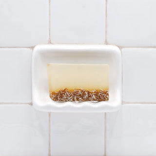 Lavender Oatmeal Vegetable Glycerin Bar Soap in a white soap dish on a tiled bathroom wall.