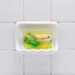 Lemongrass & Cranberry Seeds Vegetable Glycerin Bar Soap in a white soap dish on a tiled bathroom wall.