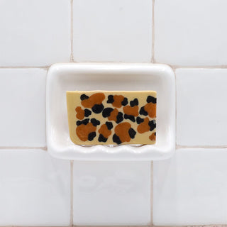Leopard Vegetable Glycerin Bar Soap in a white soap dish on a tiled bathroom wall.