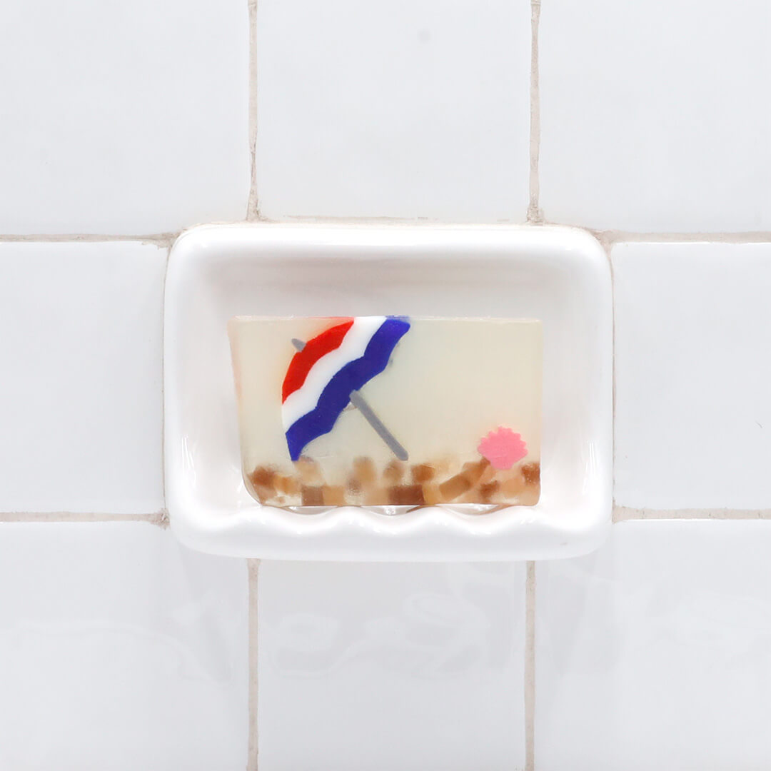 Life's a Beach Vegetable Glycerin Bar Soap in a white soap dish on a tiled bathroom wall.