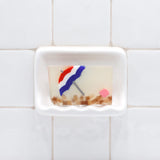 Life's a Beach Vegetable Glycerin Bar Soap in a white soap dish on a tiled bathroom wall.