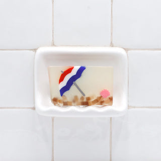 Life's a Beach Vegetable Glycerin Bar Soap in a white soap dish on a tiled bathroom wall.