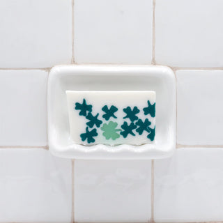 Lil' Bit of Luck Vegetable Glycerin Bar Soap in a white soap dish on a tiled bathroom wall.