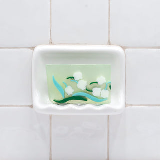 Lily of the Valley Vegetable Glycerin Bar Soap in a white soap dish on a tiled bathroom wall.