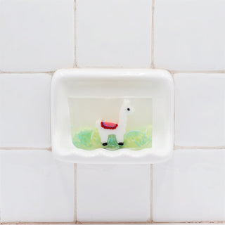 Llama Vegetable Glycerin Bar Soap in a white soap dish on a tiled bathroom wall.